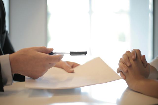One person passing another person a contract over a table.