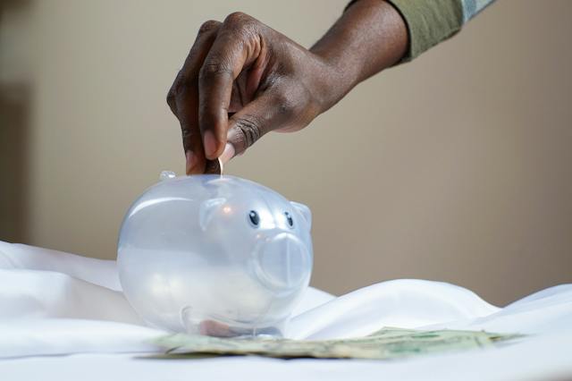 A hand dropping a coin into a piggybank.