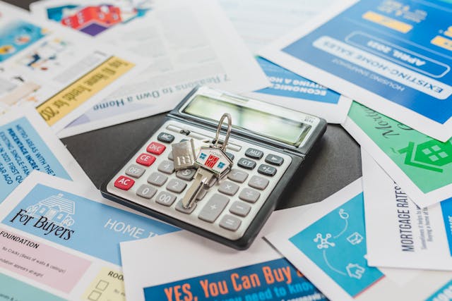 calculator and house keys on top of financial flyers and documents