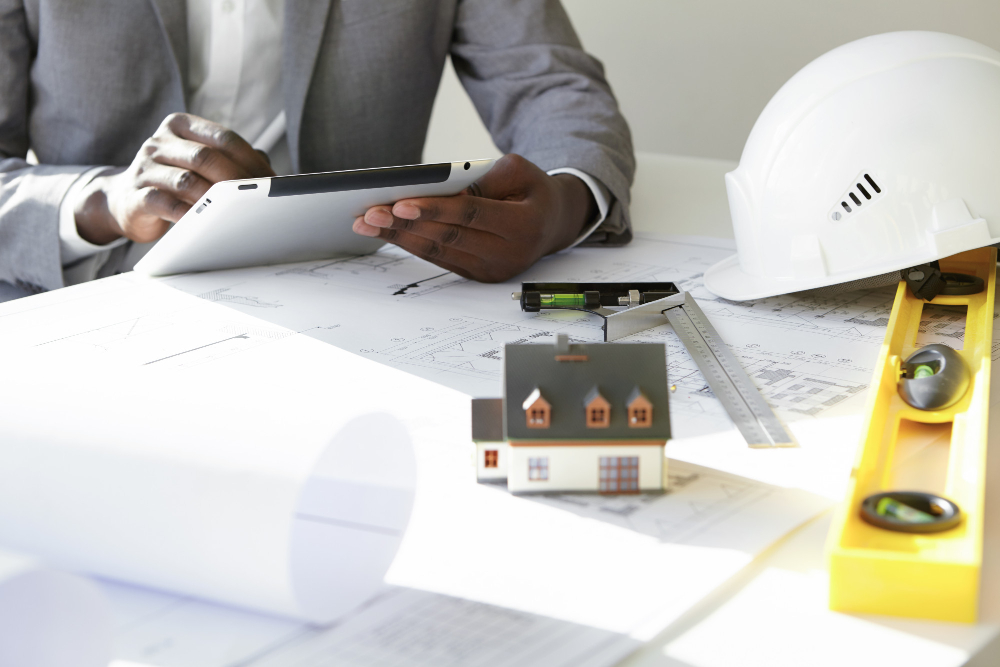 blueprints hard hat and person holding tablet at table