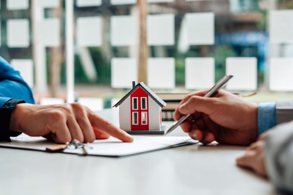 a house figurine and someone pointing to a contract